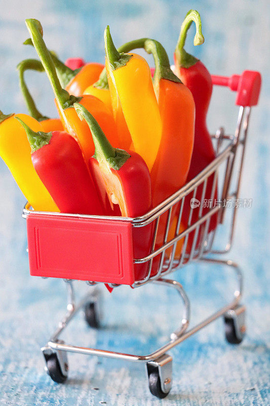一组红、黄、橙迷你辣椒(Capsicum annuum)的全画幅图像，模型购物车，健康食品店，斑驳的蓝色背景，重点放在前景，健康饮食理念